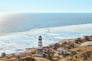 atmosphärischer romantischer blick auf den weiß-roten leuchtturm mit landwirtschaftlichen wirtschaftshäusern in merzhanovo foto