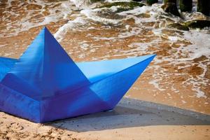 Origami blaues Papierboot am Sandstrand für Konzeptdesign, schönes Papierschiff am Ufer, Nahaufnahme foto