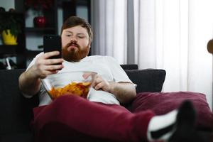 Mann, der Chips isst, während er sein Telefon überprüft foto