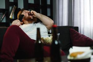 dicker Mann isst Popcorn auf dem Sofa foto