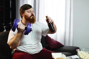 Mann, der ein Bier trinkt und Gewichte hebt foto