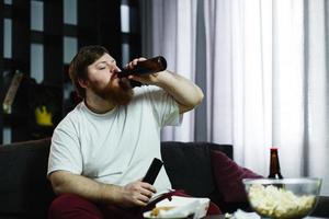 dicker Mann trinkt Bier, das auf dem Sofa liegt foto