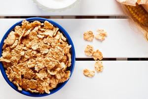 Cornflakes in einer blauen Schüssel auf weißem Holztisch mit Maiskolben und Zucker. horizontales Bild. foto