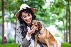 glückliche hipster-frau, die mit ihrem hund spielt und kaffee trinkt. stilvolles mädchen mit lustigem hund, der sich ausruht, umarmt und spaß in der sonne hat, süße momente. Platz für Text foto