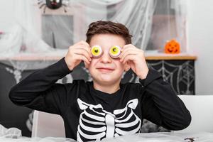 glücklicher halloween attraktiver kleiner junge im kostüm hat spaß und spielt mit gruseliger augendekoration foto