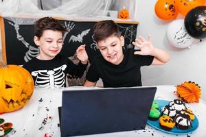 Fröhliche Jungen, Brüder, die am Halloween-Tag mit Großeltern per Videoanruf mit Laptop sprechen, aufgeregte Jungen in Kostümen, die winkend und lächelnd auf den Computer schauen. foto