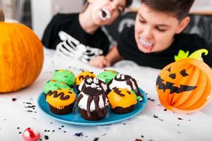 kinder, die spaß für halloween haben, umgeben von gruseliger dekoration. Jack o' Lantern Halloween-Kürbis und Cupcakes auf dem Tisch. Fröhliches Halloween foto