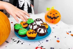 kinderhand greift nach halloween-dekoriertem cupcake auf dem tisch. Fröhliches Halloween foto