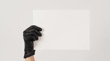 eine hand hält das a4-papier und trägt latexhandschuhe auf weißem hintergrund. foto