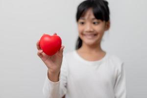 Porträt des asiatischen kleinen Mädchens, das rotes Herzzeichen auf weißem Hintergrund hält foto