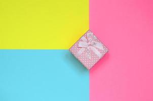kleine rosa geschenkbox liegen auf texturhintergrund von modepastellblauem, gelbem und rosafarbenem papier in minimalem konzept foto