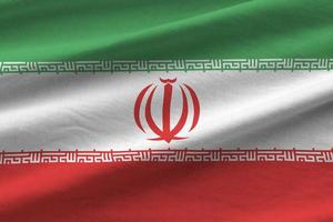 iranische flagge mit großen falten, die unter dem studiolicht im innenbereich winken. die offiziellen symbole und farben im banner foto