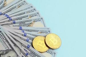 goldene bitcoins und hundertdollarscheine liegen auf hellblauem hintergrund foto