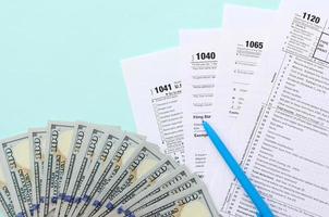 Steuerformulare liegen in der Nähe von Hundertdollarscheinen und blauem Stift auf hellblauem Hintergrund. Einkommensteuerrückerstattung foto