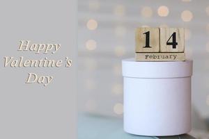 Valentinstag-Konzept. datum 14. februar auf hölzernem rotem würfelkalender auf einer weißen geschenkbox. Bokeh goldener und weißer Hintergrund. foto