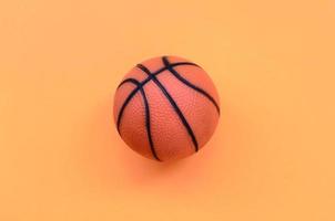 kleiner orangefarbener ball für basketballsportspiel liegt auf texturhintergrund von modepastellorangefarbenem papier in minimalem konzept foto