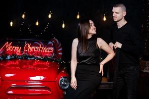 junges glückliches paar mann und frau, die sich in weihnachten verliebt haben, umarmen sich in der nähe eines roten retro-autos mit neujahrsgeschenken. kuss, mädchen, glück, quarantäne weihnachtsfeier, urlaub foto