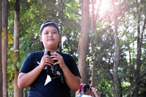 südostasiatische jungen benutzen ferngläser, um vögel im tropischen wald zu beobachten, idee zum lernen von kreaturen und wild lebenden tieren außerhalb des klassenzimmers. foto