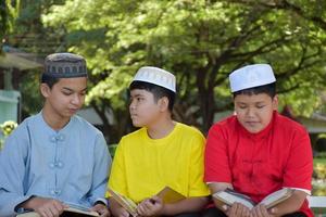 Eine Gruppe muslimischer Jungen sitzt zusammen unter dem Baum im Schulpark, sie lesen, lernen, reden, schlagen vor und beraten sich gegenseitig über Lernprobleme, weicher und selektiver Fokus. foto