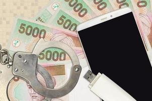 5000 indonesische Rupiah-Scheine und Smartphone mit Polizeihandschellen. Konzept von Hacker-Phishing-Angriffen, illegalem Betrug oder weicher Verteilung von Malware foto