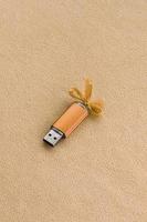 Orangefarbene USB-Flash-Speicherkarte mit blauer Schleife liegt auf einer Decke aus weichem und pelzigem, hellorangefarbenem Fleece-Stoff. klassisches weibliches Geschenkdesign für eine Speicherkarte foto