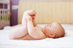 glückliches Baby, das mit seinen Füßen auf weißem Hintergrund spielt. Porträt eines süßen, glücklichen Babys