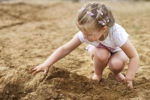 ein kleines Kind spielt im Sand. schönes Mädchen, das am Strand sitzt. foto