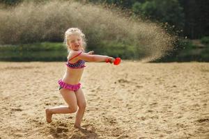 Mädchen wirft Sand. schönes Mädchen, das mit Sand am Strand spielt. Kind hat Spaß. Urlaubsglück und Freiheitskonzept. foto