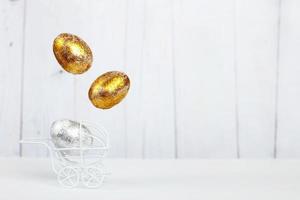 ostern goldene und silberne eier schweben im weißen kinderwagen auf hellem holzhintergrund. Neugeborenes Konzept foto