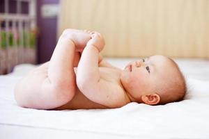 glückliches Baby, das mit seinen Füßen auf weißem Hintergrund spielt. Porträt eines süßen, glücklichen Babys foto