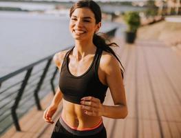 aktive junge schöne Frau, die auf der Promenade entlang des Flussufers läuft foto