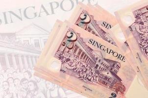 2 Singapur-Dollar-Scheine liegen im Stapel auf dem Hintergrund einer großen halbtransparenten Banknote. abstrakte Darstellung der Landeswährung foto