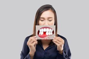 asiatische frau im dunkelblauen hemd, das ein braunes papier mit dem gebrochenen zahnkarikaturbild seines mundes hält foto