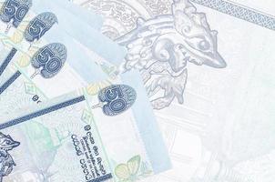 50 srilankische Rupien-Scheine liegen im Stapel auf dem Hintergrund einer großen halbtransparenten Banknote. abstrakter betriebswirtschaftlicher hintergrund foto
