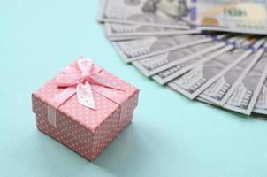 Rosa gepunktete Geschenkbox liegt in der Nähe von Hundert-Dollar-Scheinen auf hellblauem Hintergrund foto