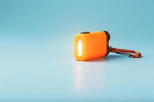 Eine orange LED-Taschenlampe mit Karabiner leuchtet auf blauem Hintergrund. foto