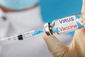 eine Ampulle mit der Aufschrift Virusimpfstoff und eine Spritze in den Händen eines wissenschaftlichen Arztes in Gummihandschuhen mit einer Impfstoffnahaufnahme.