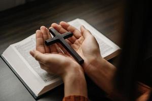 frau, die sitzt und die schriften studiert. das holzkreuz in den händen. christliche bildungskonzepte öffnen die heilige schrift foto