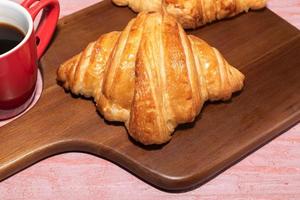 frühstückscroissant im schneidebrett und kaffee auf holztisch. foto