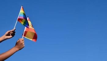 spanien-flagge und regenbogenflagge, lgbt-symbol, in händen halten, blauer hintergrund, konzept für lgbt-feiern in spanien und auf der ganzen welt im stolzmonat, juni, weicher und selektiver fokus, kopierraum.