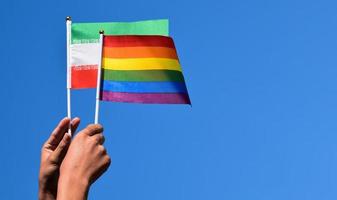 iranische flagge und regenbogenflagge, lgbt-symbol, in händen halten, blauer hintergrund, konzept für lgbt-feier im iran und auf der ganzen welt im stolzmonat, juni, weicher und selektiver fokus, kopierraum. foto