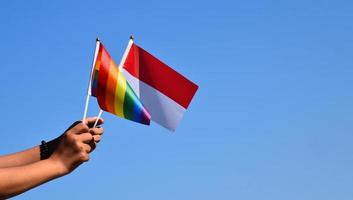 indonesien-flagge und regenbogenflagge, lgbt-symbol, in den händen halten, blauer hintergrund, konzept für lgbt-feiern in indonesien und auf der ganzen welt im stolzmonat, juni, weicher und selektiver fokus. foto