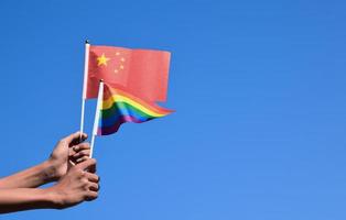 china-flagge und regenbogenflagge, lgbt-symbol, in händen halten, blauer hintergrund, konzept für lgbt-feiern in china und auf der ganzen welt im stolzmonat, juni, weicher und selektiver fokus, kopierraum.