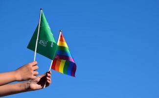 saudi-arabien-flagge und regenbogenfahne, lgbt-symbol, in händen halten, blauer himmelshintergrund, konzept für lgbt-feier in saudi-arabien im stolzmonat, juni, weicher und selektiver fokus. foto