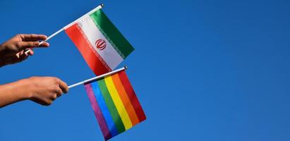 iranische flagge und regenbogenflagge, lgbt-symbol, in händen halten, blauer hintergrund, konzept für lgbt-feier im iran und auf der ganzen welt im stolzmonat, juni, weicher und selektiver fokus, kopierraum.