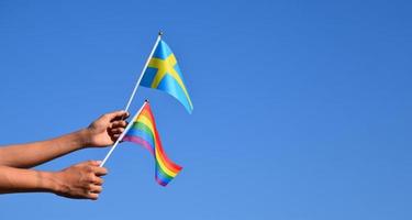 schwedenfahne und regenbogenfahne, lgbt-symbol, in händen halten, blauer hintergrund, konzept für lgbt-feiern in schweden und auf der ganzen welt im stolzmonat, juni, weicher und selektiver fokus, kopierraum. foto