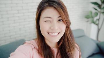 asiatische bloggerin, die zu hause im wohnzimmer vlog-videos mit dem smartphone aufzeichnet, genießen sie lustige momente, während sie auf dem sofa liegen, wenn sie sich zu hause entspannen. Lifestyle-Blogger, der zu Hause Videos macht. foto