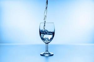 Spritzwasser aus Glas isoliert auf blauem Hintergrund foto