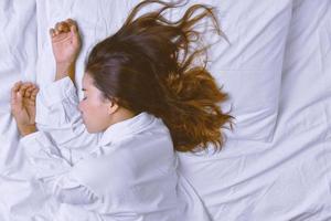 junge Frau, die im Bett schläft. Blick von oben auf die junge Frau, die sich hinlegt und gut im Bett schläft. Schlafen entspannen, junge lächelnde hübsche Dame liegt im Bett. entspannen, schlafen. foto