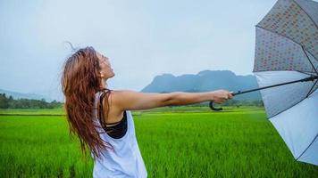 asiatische frauen reisen im urlaub entspannen. Die Frauen standen glücklich mit einem Regenschirm im Regen und genießen den Regen, der fällt. Reisen in Länder, grüne Reisfelder, Reisen durch Thailand. foto